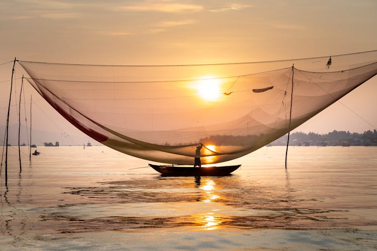 Unrecognizable Fisherman In Boat On Lake Under Net In Evening