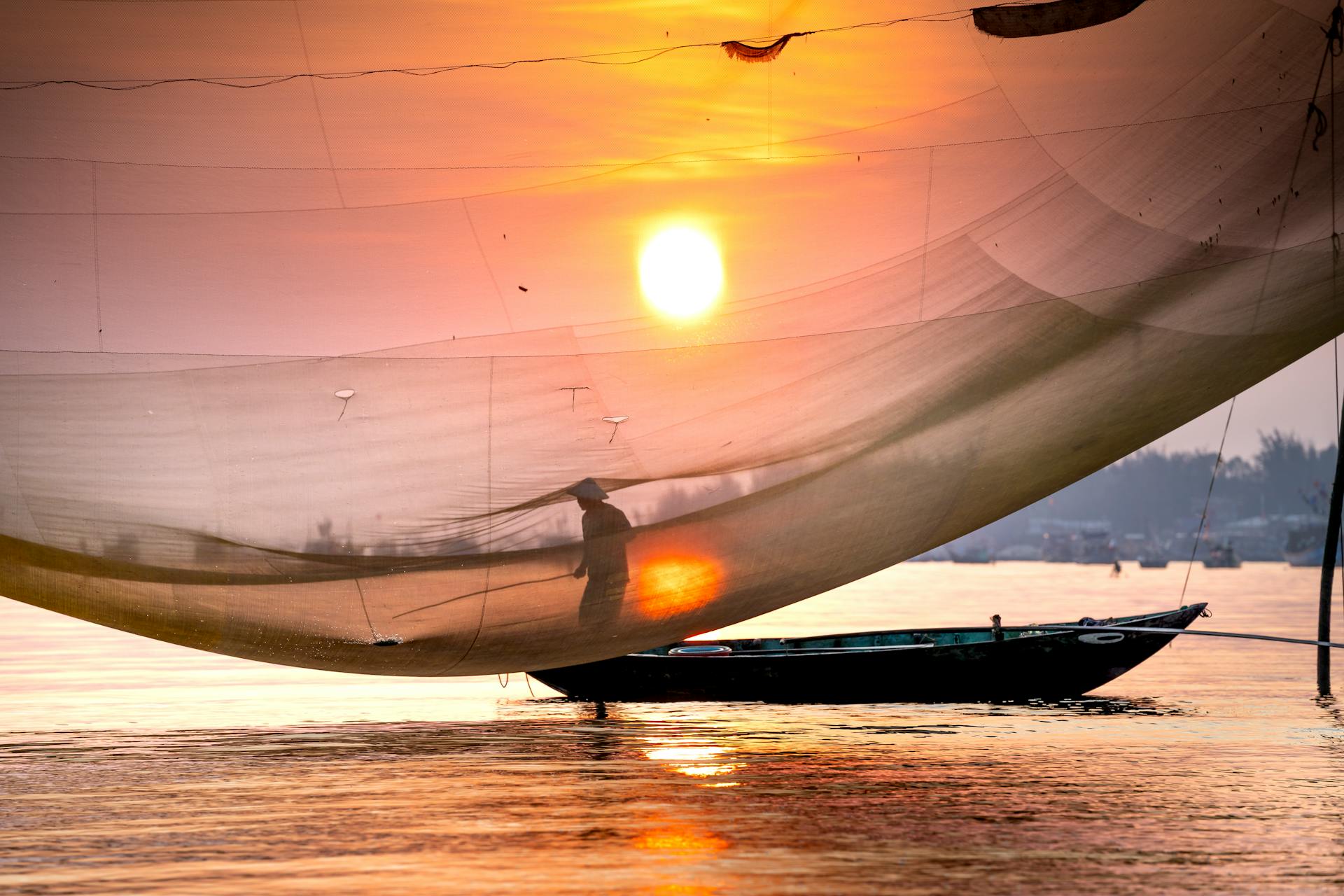 Anonymous fisher with net catching fish from boat on river