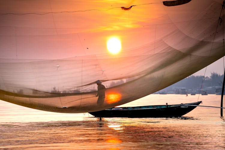 Anonymous Fisher With Net Catching Fish From Boat On River