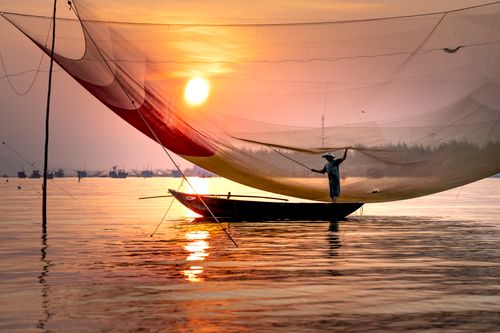 Free Unrecognizable male fisher in boat on rippled river under fishing net and shiny sun in evening sky Stock Photo
