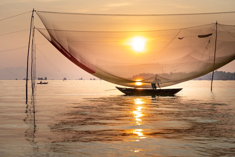 Silhouette Of Fisherman In Boat Catching Fish With Large Net