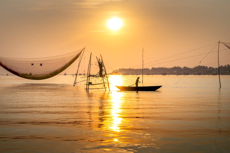 Anonymous Man Rowing Boat Near Fishing Net At Sundown