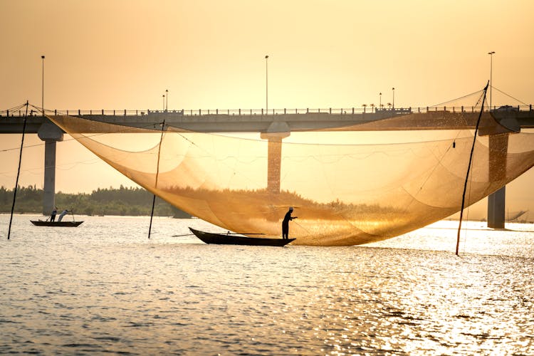 Faceless Fishermen Catching Fish With Large Traditional Net In River At Sundown