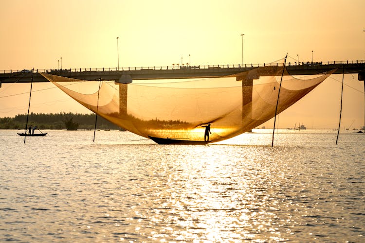 Fishermen In Boats On River Catching Fish With Large Lift Nets At Sundown