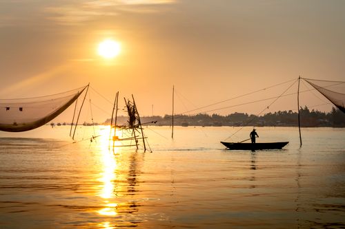 Free Silhouette of anonymous person rowing boat near fishing nets on river reflecting bright sunset sky in Vietnam Stock Photo