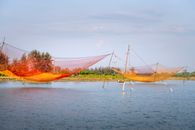 Large colorful lift fishing nets stretched between bamboo poles over rippling river flowing in Hoi An