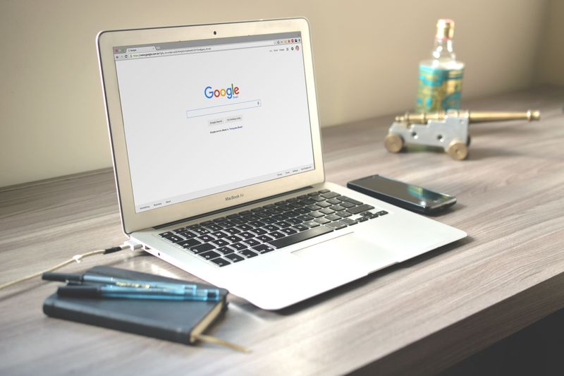 A neat workspace featuring a laptop displaying Google search, a smartphone, and a notebook on a wooden desk.