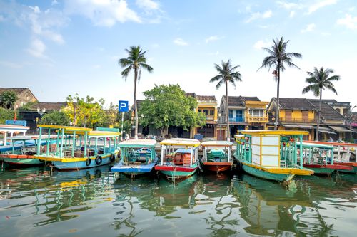 Free Colorful excursion boats moored on river near embankment near palm trees and typical houses on sunny day in Hoi An Stock Photo