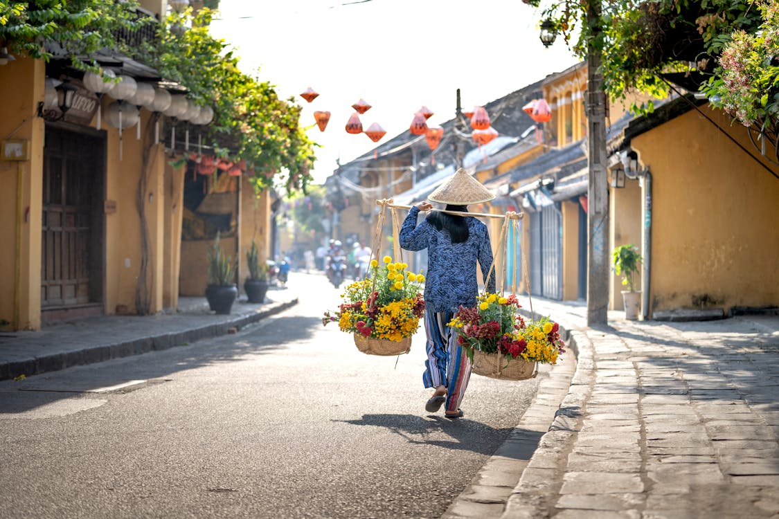 Free Faceless Asian female flower seller with baskets strolling in town Stock Photo