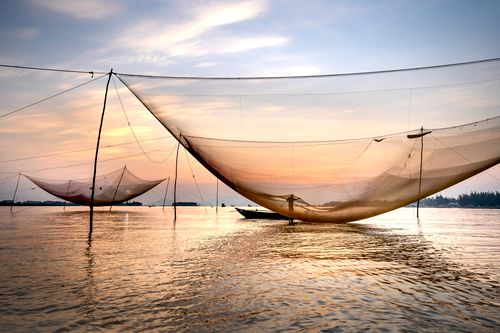 Free Silhouette of distant unrecognizable man floating on boat on rippling sea near fishing nets while catching fish in evening time Stock Photo