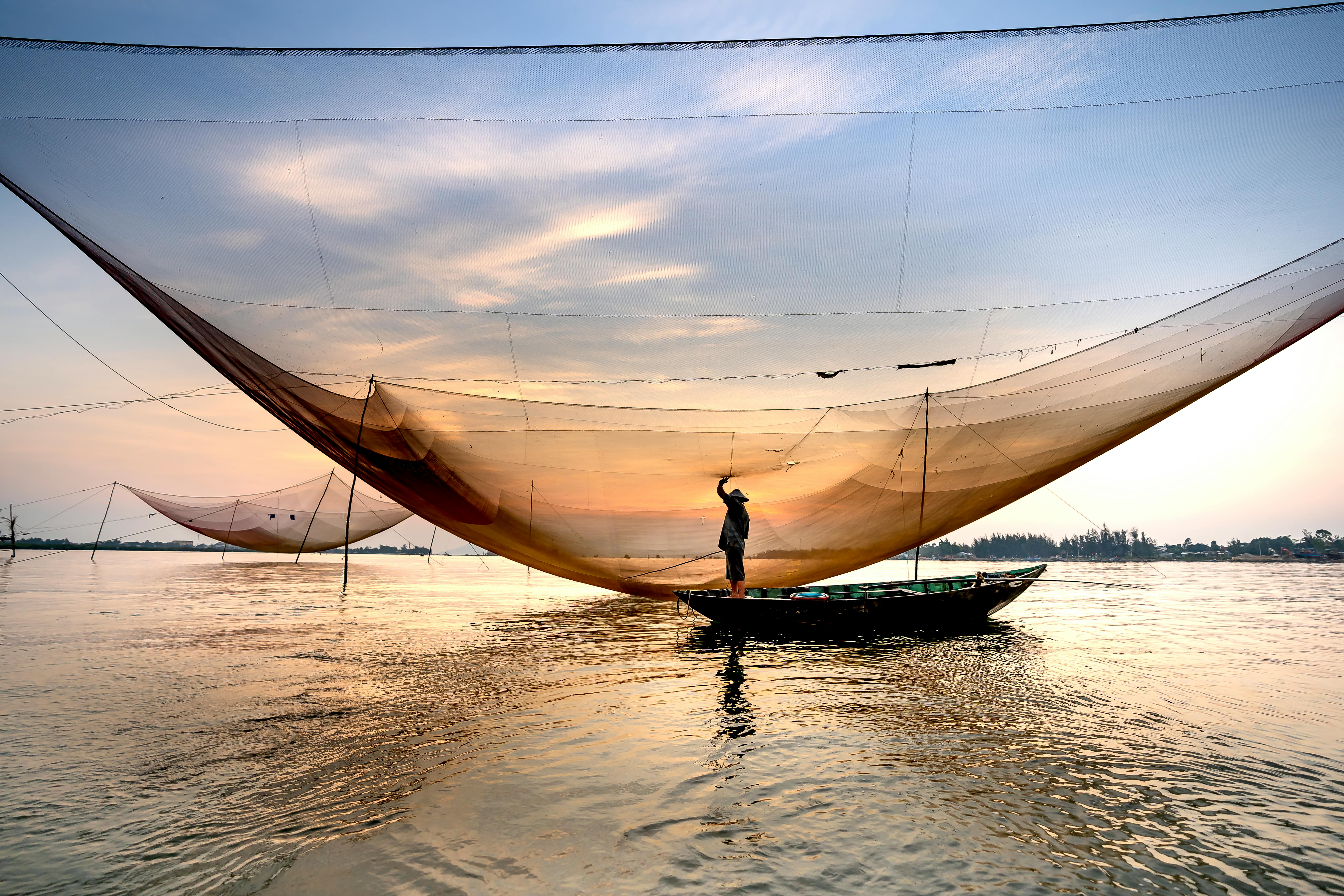 Anonymous fisherman standing in boat or river near fishing net