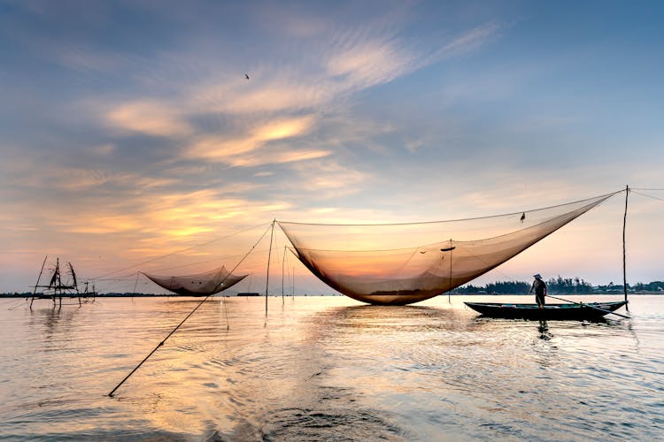 Unrecognizable Male Angler Floating In Boat On River While Catching Fish With Nets