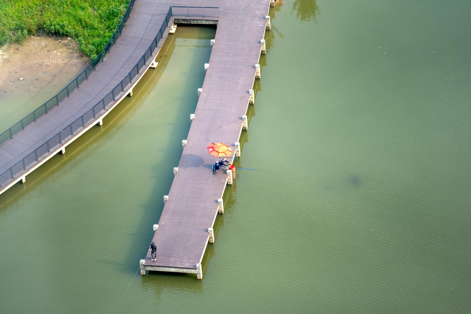 Drone view of people on wooden pier with rods catching fish in shallow water of river