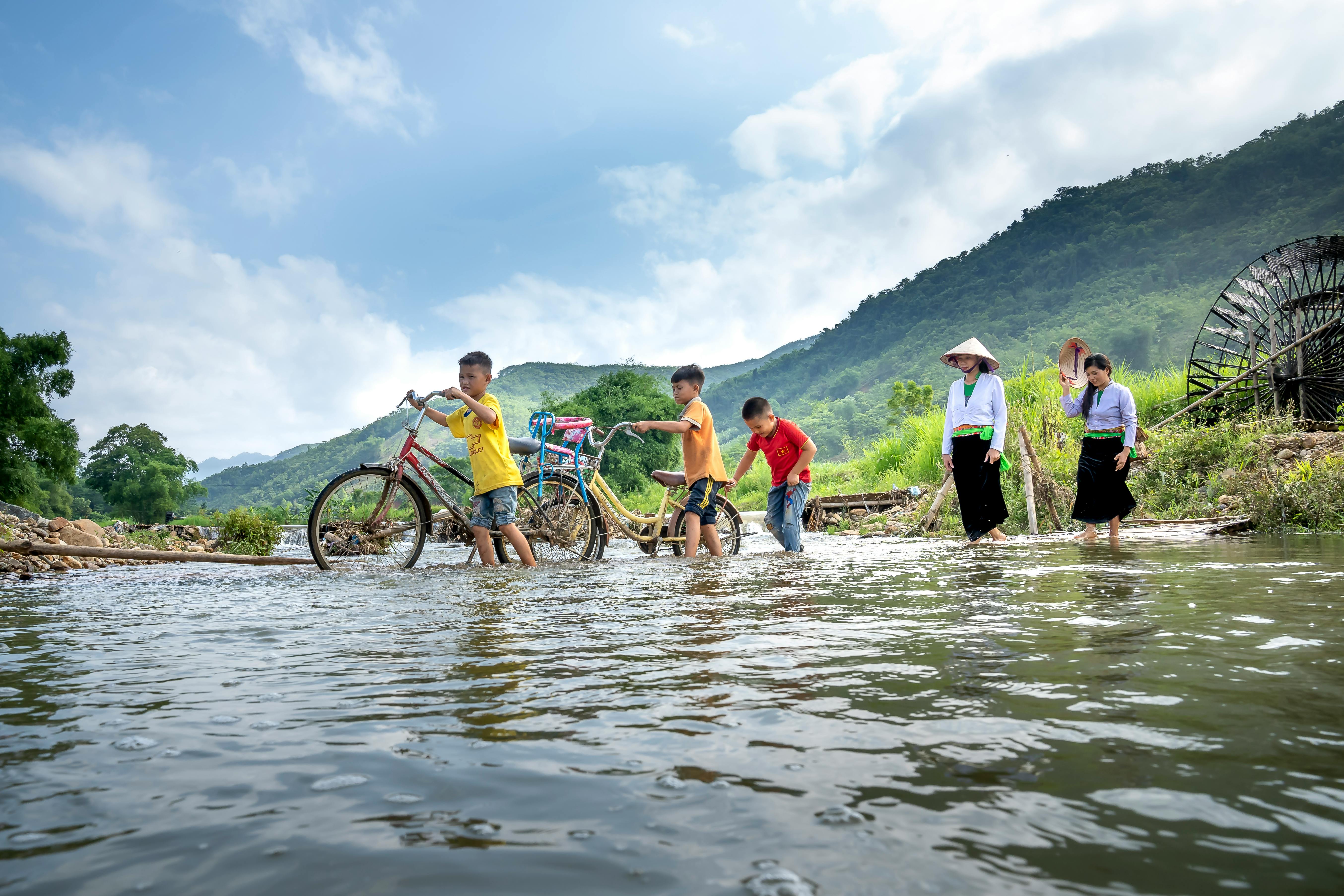 group of ethnic kids and women crossing river