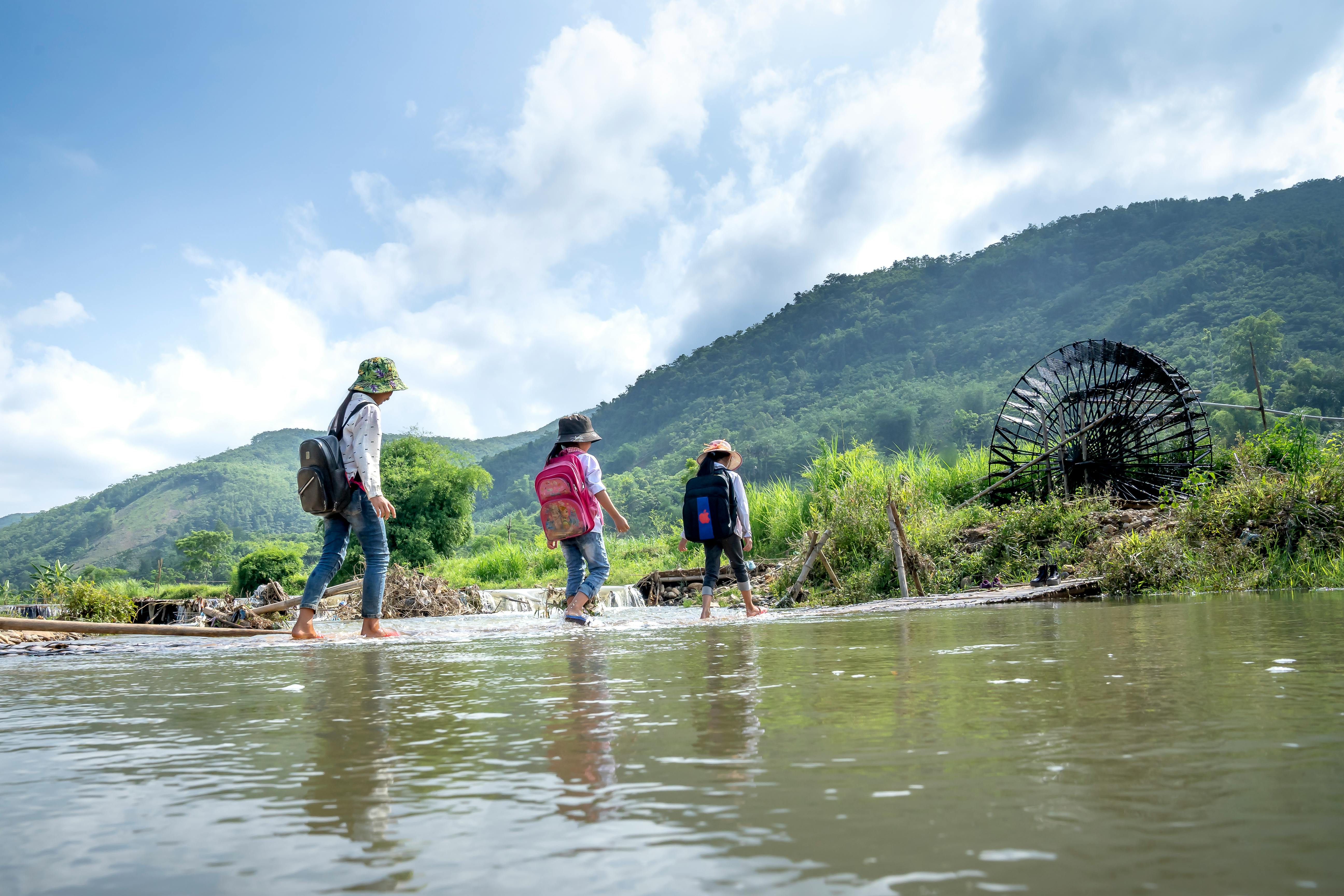 kids with backpacks crossing river in nature