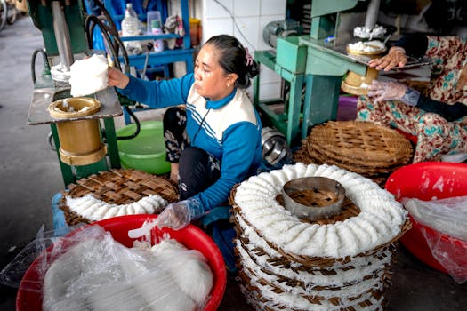 Woman crafting traditional noodles in an open market setting.
