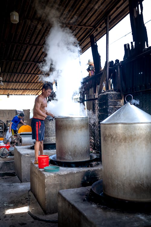 Male wearing shorts while making noodle in metal barrels and machines on manufacture in Vietnam