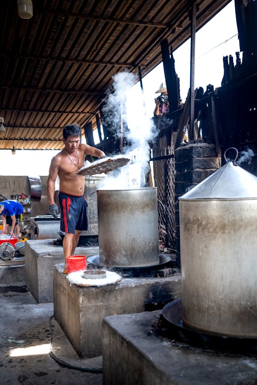 Free Guy standing near metal barrels and machines while making noodle on caps in Vietnam in factory Stock Photo