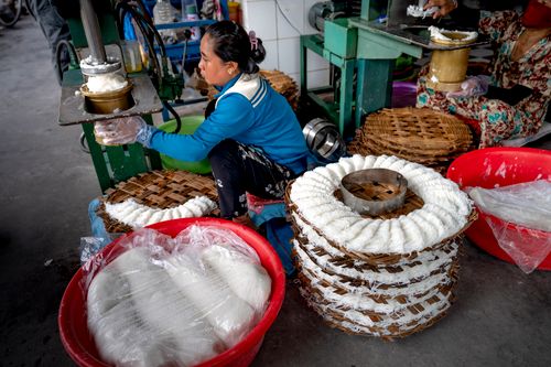 Free A woman prepares traditional rice noodles using a press machine in an outdoor setting. Stock Photo