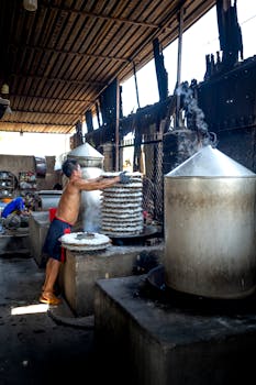 Full length of man standing near metal barrels and machines while making noodle on caps in factory in Vietnam
