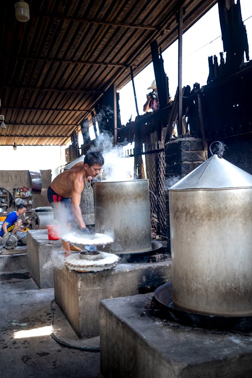 Male wearing shorts while making noodle near metal barrels and machines on manufacture in Vietnam