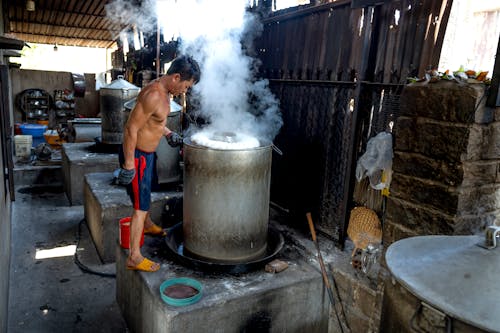 Free Full length of male in shorts while making noodle on caps in metal barrels and machines on manufacture in Vietnam Stock Photo