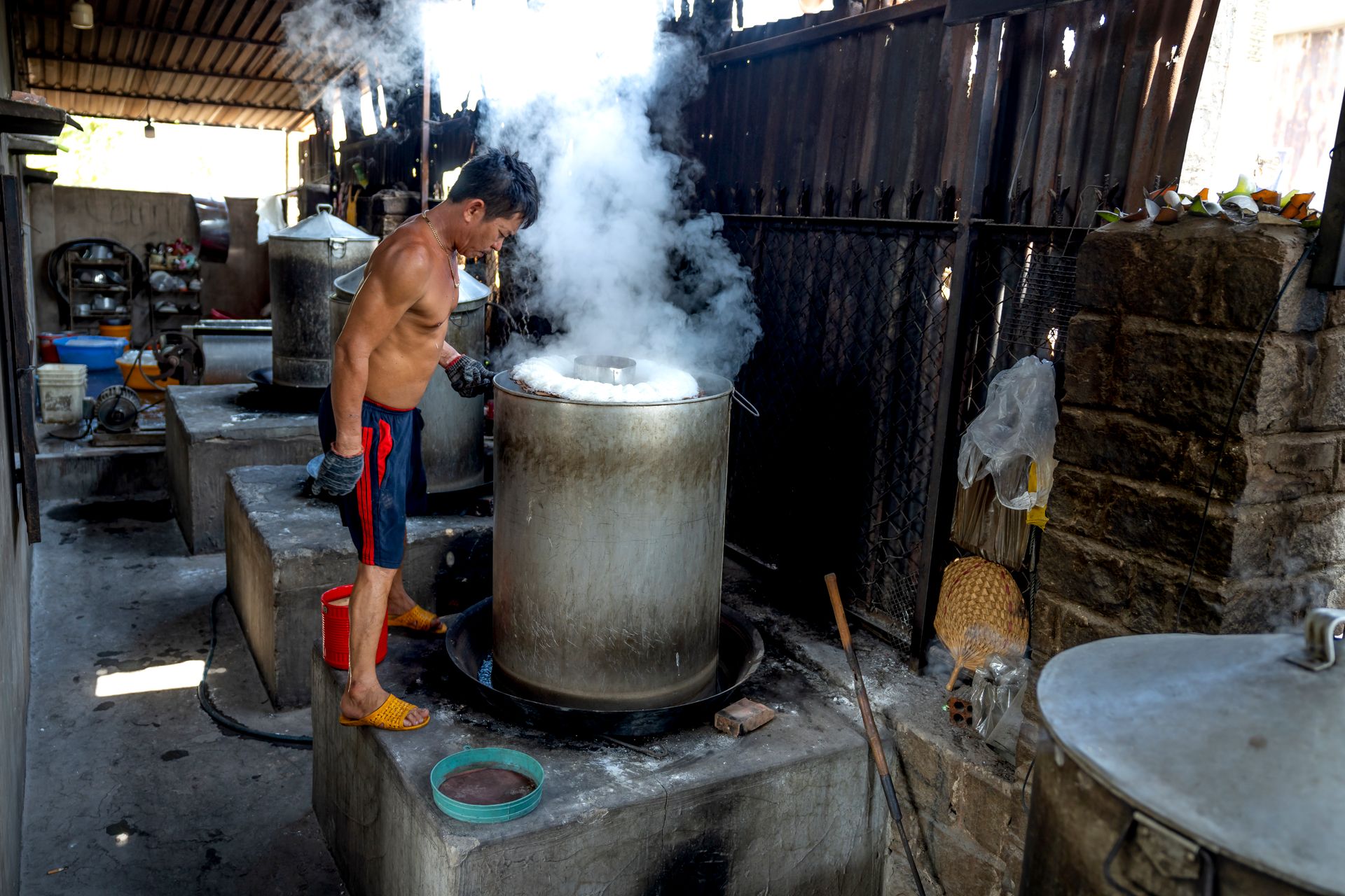 Full length of male in shorts while making noodle on caps in metal barrels and machines on manufacture in Vietnam
