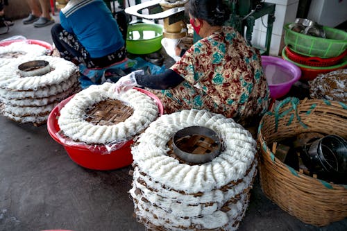 Crop unrecognizable workers in casual clothes making noodle on caps while sitting near basins and metal machine on manufacture in Vietnam