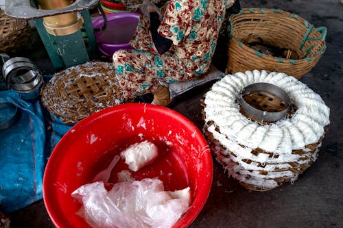 From above of tool for production of traditional Vietnamese noodles with white dough near plastic container and wicker basket