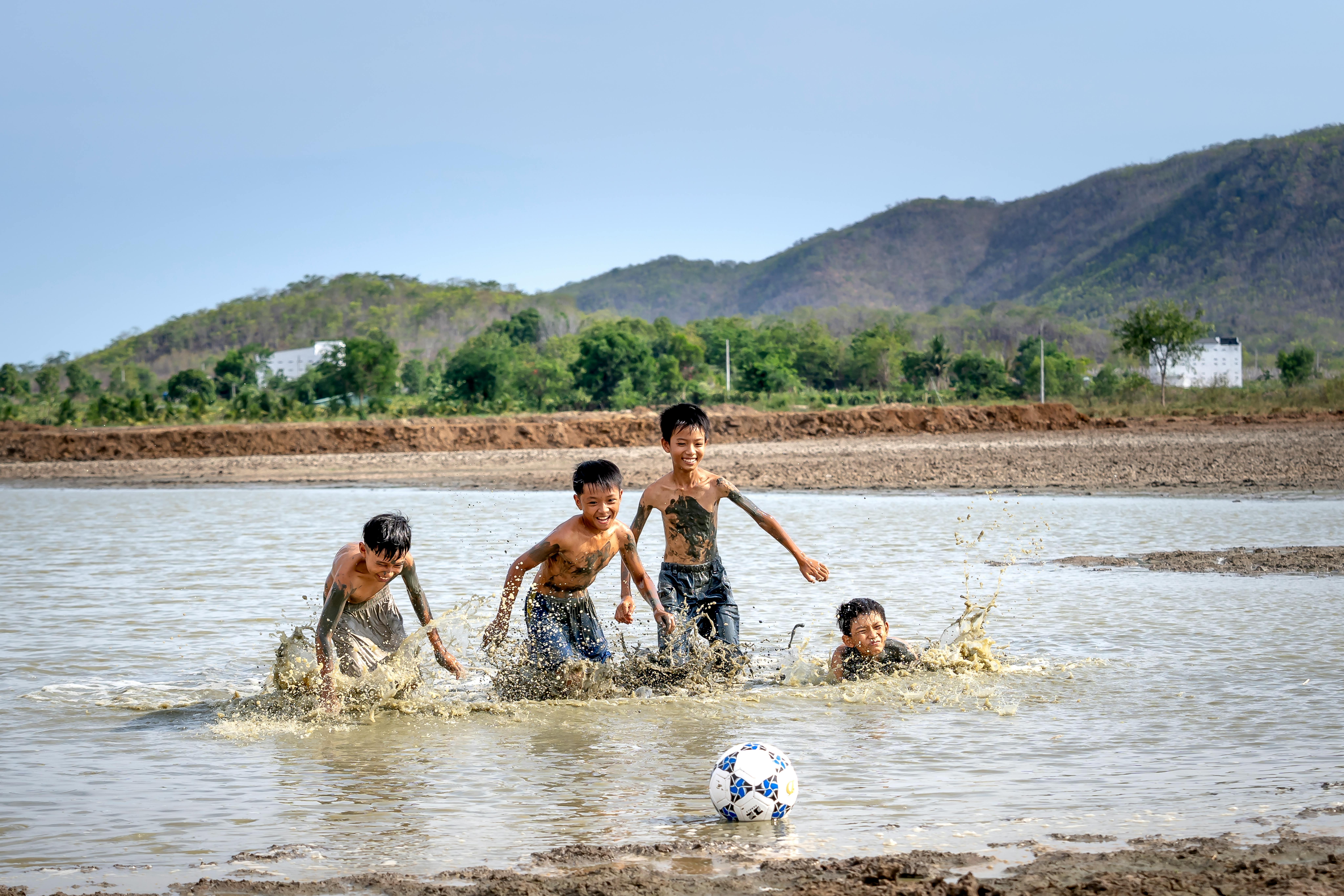 smiling asian boys playing with ball on river
