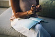 Close-Up Shot of a Woman Holding a Pen and a Book on her Lap