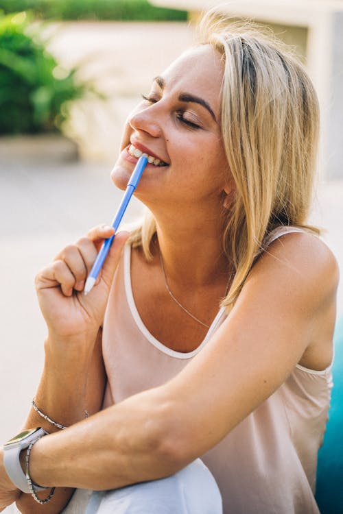 Close-Up Shot of a Woman in a White Tank Top Holding a Blue Pen