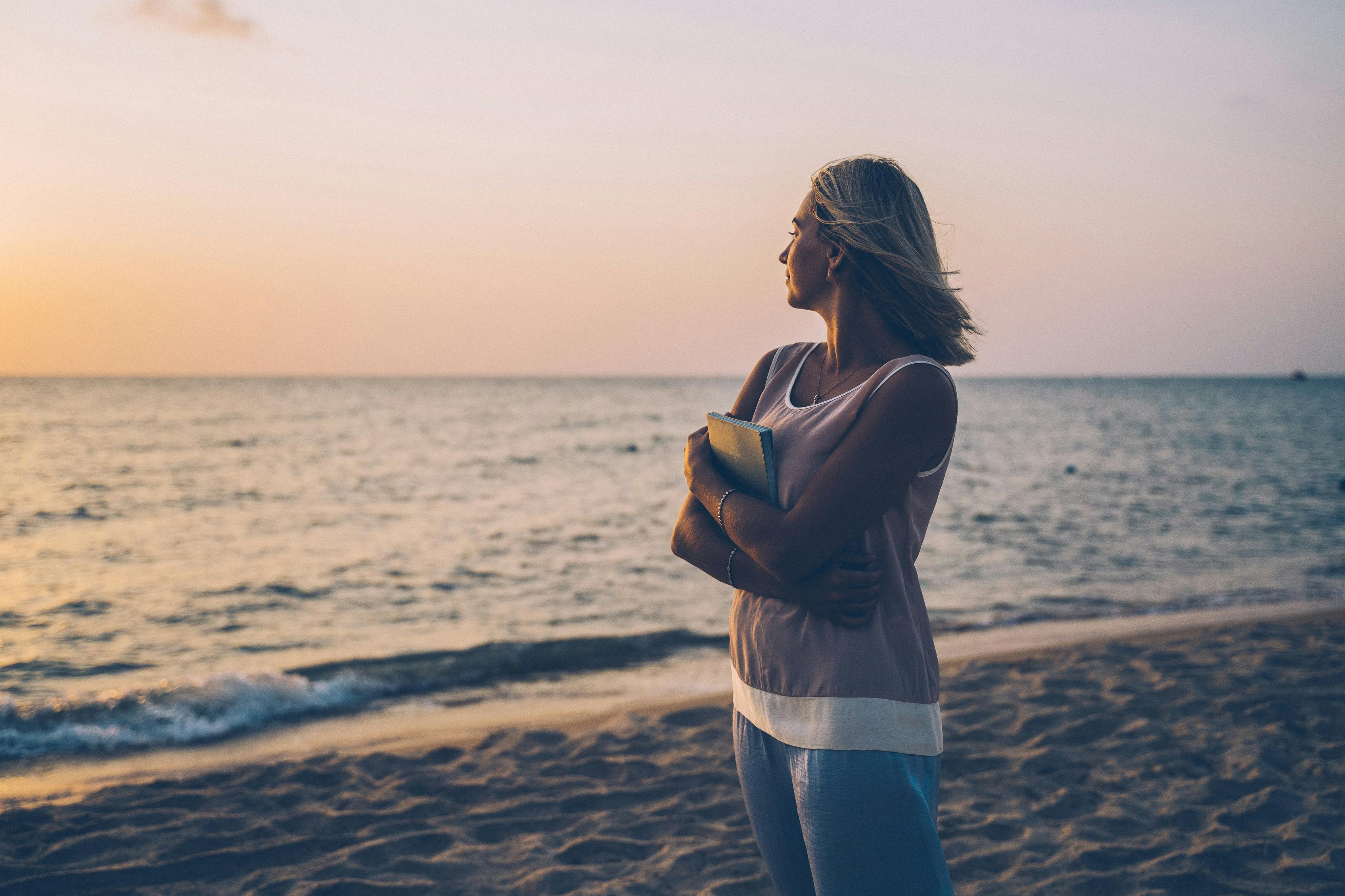 woman wearing sleeveless top standing on the beach during sunset