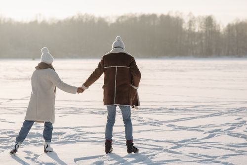Free Romantic couple ice skating on a sunlit frozen lake during winter, wearing cozy jackets and hats. Stock Photo