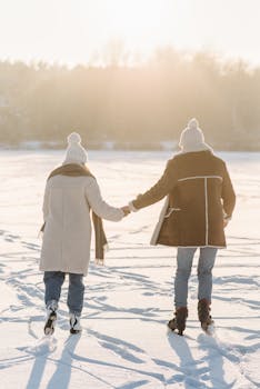 Couple ice skating, hand in hand, on a sunlit frozen lake during winter.