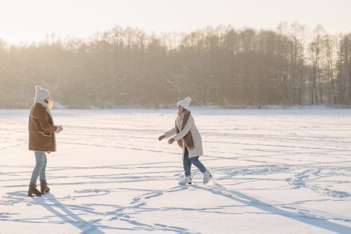 Free A couple enjoys ice skating on a frozen lake, surrounded by snow and trees in winter. Stock Photo