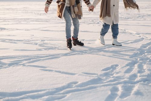 Free A couple holding hands while ice skating on a snowy winter day, creating a romantic scene. Stock Photo