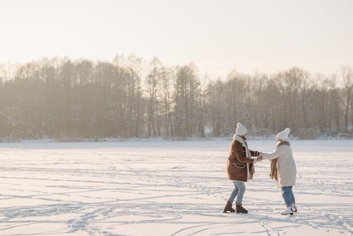 Free Happy couple enjoying ice skating on a frozen lake amidst a tranquil winter landscape. Stock Photo
