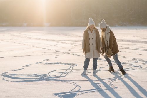 Free Two friends enjoy a sunny winter day, playfully making snow angels on a vast snowy field. Stock Photo