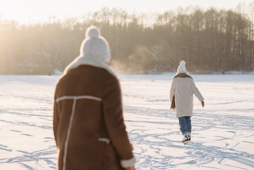Free Two adults ice skating on a snowy frozen lake surrounded by trees. Stock Photo