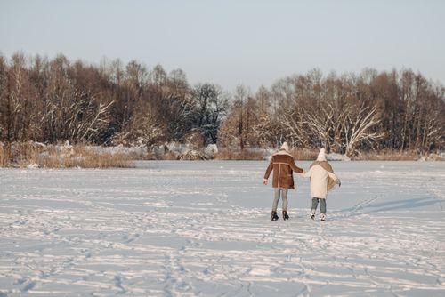 Free Two adults ice skating hand in hand on a snow-covered lake. Winter scenery with forest and snow. Stock Photo