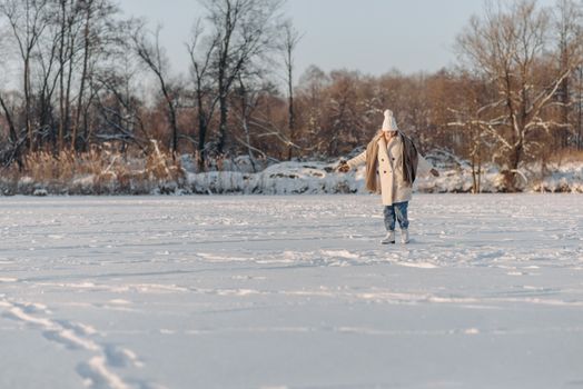 Stylish woman in winter attire standing on a snow-covered field with trees in the background.