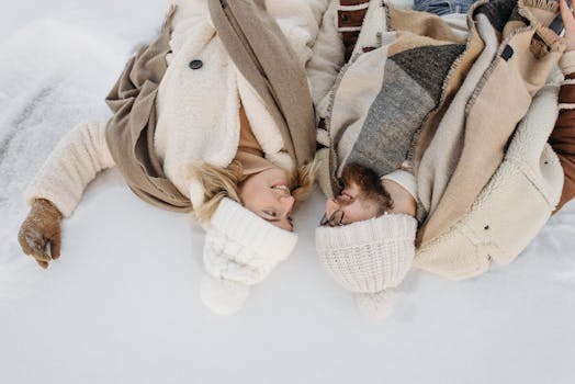 Couple enjoying togetherness in winter, lying on snowy ground with warm clothing.
