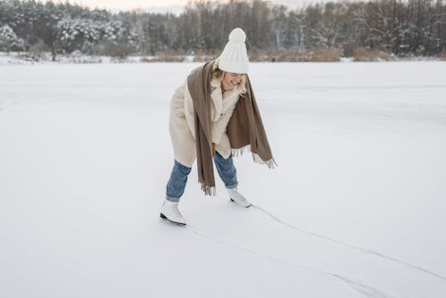 Woman in Brown Coat and White Knit Cap Standing on Snow Covered Ground