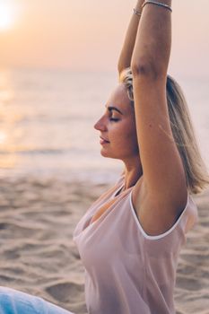 A woman practices meditation on a serene beach during sunset, embracing wellness.