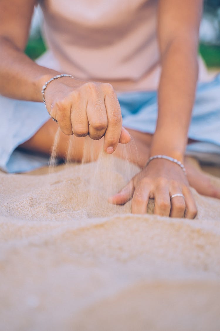 A Person Grabbing A Handful Of Sand On The Shore