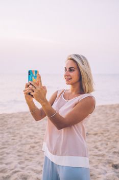 Woman takes a photo on the beach at sunset, capturing the serene and relaxed atmosphere.
