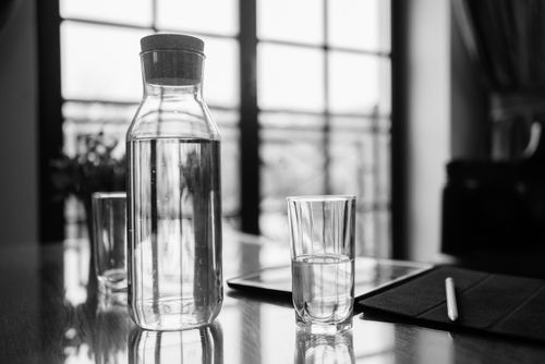 Free A minimalist black and white still life featuring a glass pitcher of water, glasses, and an iPad on a table. Stock Photo