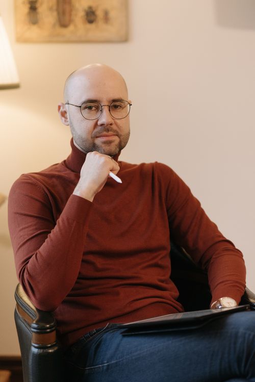 Free Professional psychologist sitting pensively in a cozy office, wearing casual attire and eyeglasses. Stock Photo