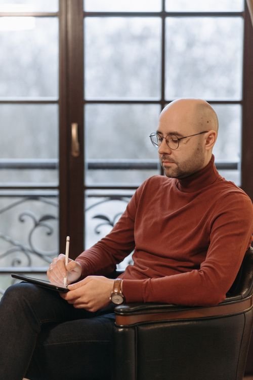 Free Bald man in glasses writing with a stylus on a tablet indoors. Stock Photo